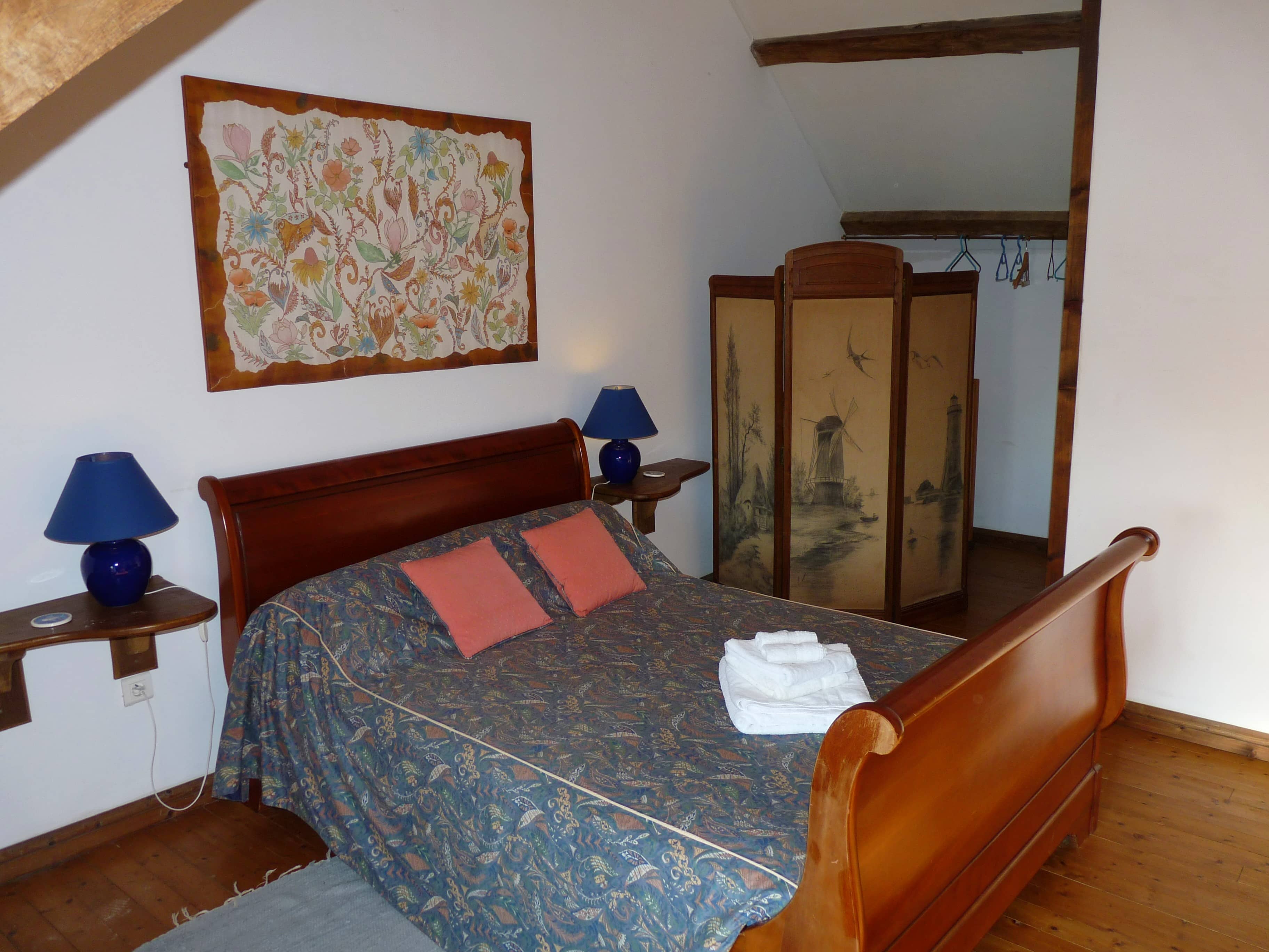 Spacious and comfortable bedroom of La Julerie cottage in Brittany, France, with a king-size bed, elegant rustic decor, a stone fireplace, and a panoramic view of the surrounding countryside. Perfect for a peaceful night's sleep after a day of sightseeing in the Brittany region.